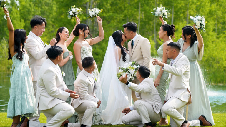Bride and groom kissing with wedding party celebrating outdoors