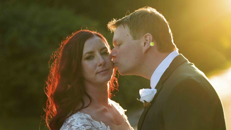 Groom kissing bride during sunset wedding portrait.