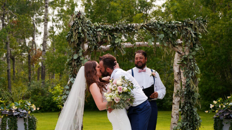Bride and groom kissing under a wedding arch.