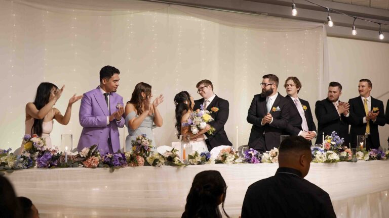 Wedding reception head table with the couple and wedding party applauding during the celebration