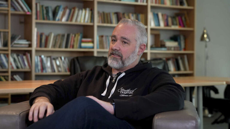 Professional interview portrait of a man seated in a lounge with bookshelves in the background
