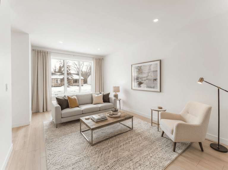 Bright staged living room with neutral sofa, accent chair, and large window
