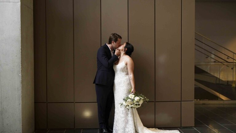 Bride and groom kissing during an indoor wedding portrait session with bouquet and modern venue backdrop