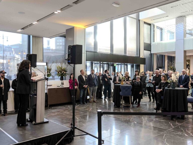 Speaker presenting at an indoor professional networking event with attendees gathered in a modern venue