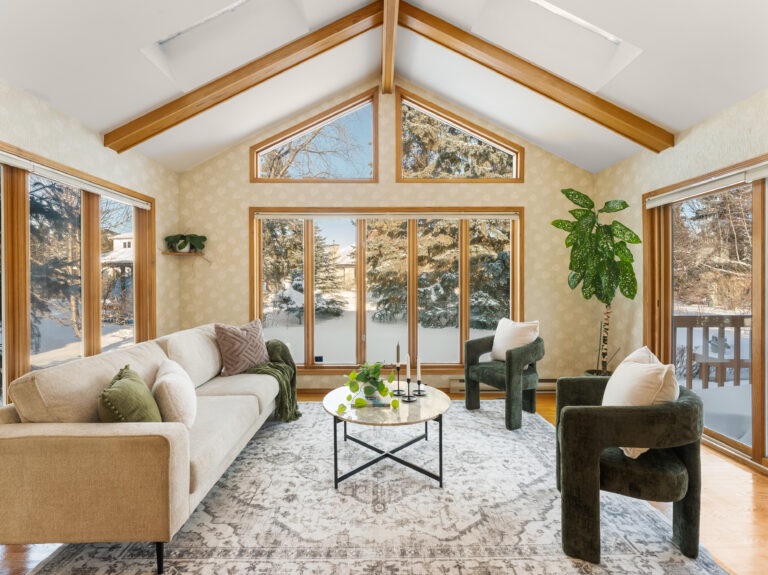 Staged living room with vaulted ceiling, wood beams, large windows, and snowy outdoor views