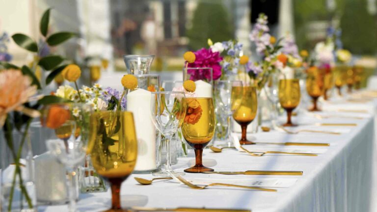 Elegant wedding reception table setting with amber glasses, candles, floral centerpieces, and gold flatware