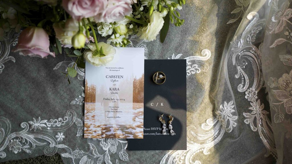 Wedding invitation flat lay with rings, earrings, floral bouquet, and lace details
