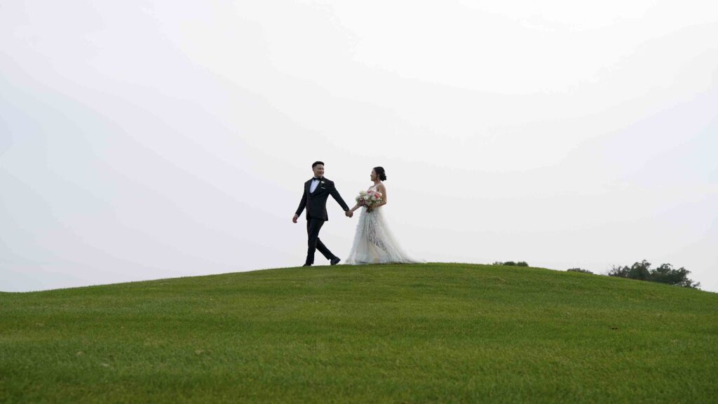 Bride and groom walking hand in hand across a grassy hilltop