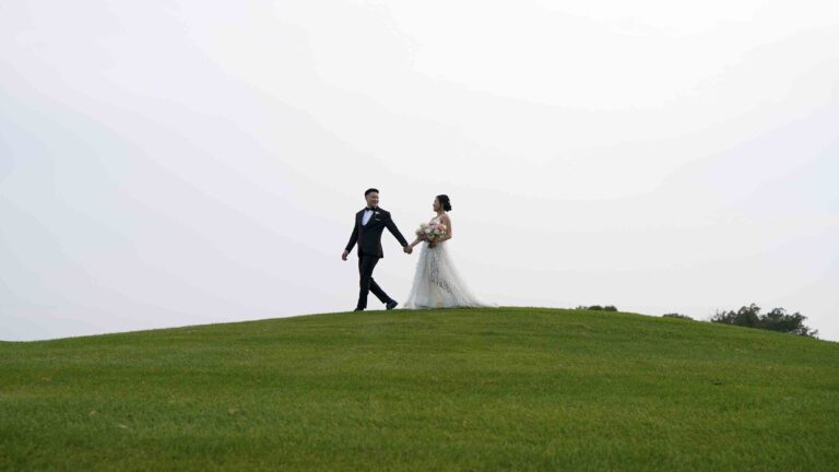 Bride and groom walking hand in hand across a grassy hilltop