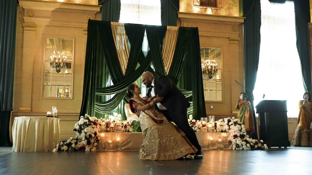 Couple dancing at an elegant wedding reception with green drapery and floral decor in Manitoba