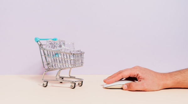 Hand using a computer mouse beside a shopping cart with money, representing website conversions