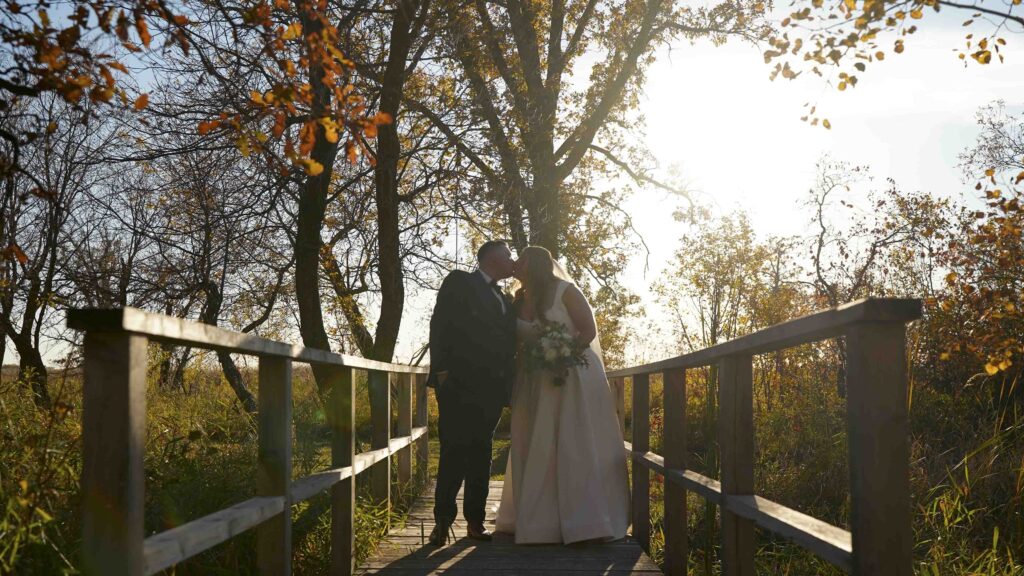 Bride and groom kissing on a wooden bridge during an outdoor Manitoba wedding