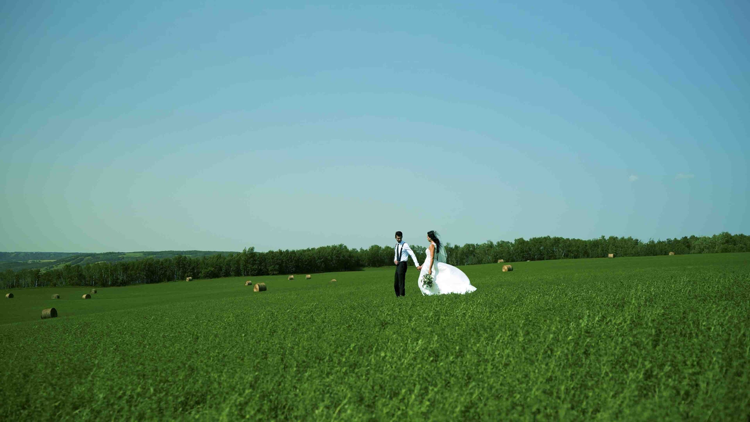 Bride and groom walking through a green field during an outdoor Manitoba wedding
