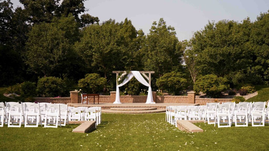 Outdoor wedding ceremony setup with white chairs and floral arch in a garden venue
