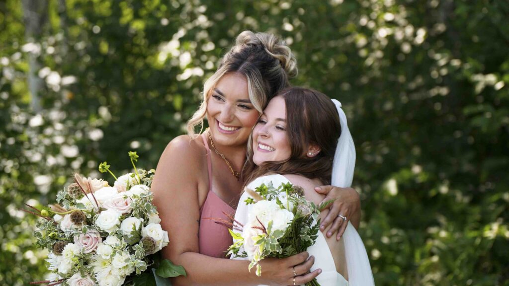 Bride and bridesmaid smiling together with wedding bouquets in an outdoor garden setting