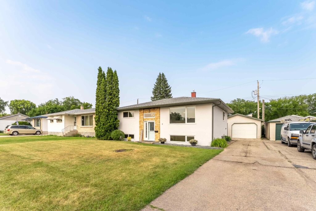 Residential home exterior with front lawn, driveway, and detached garage for real estate listing